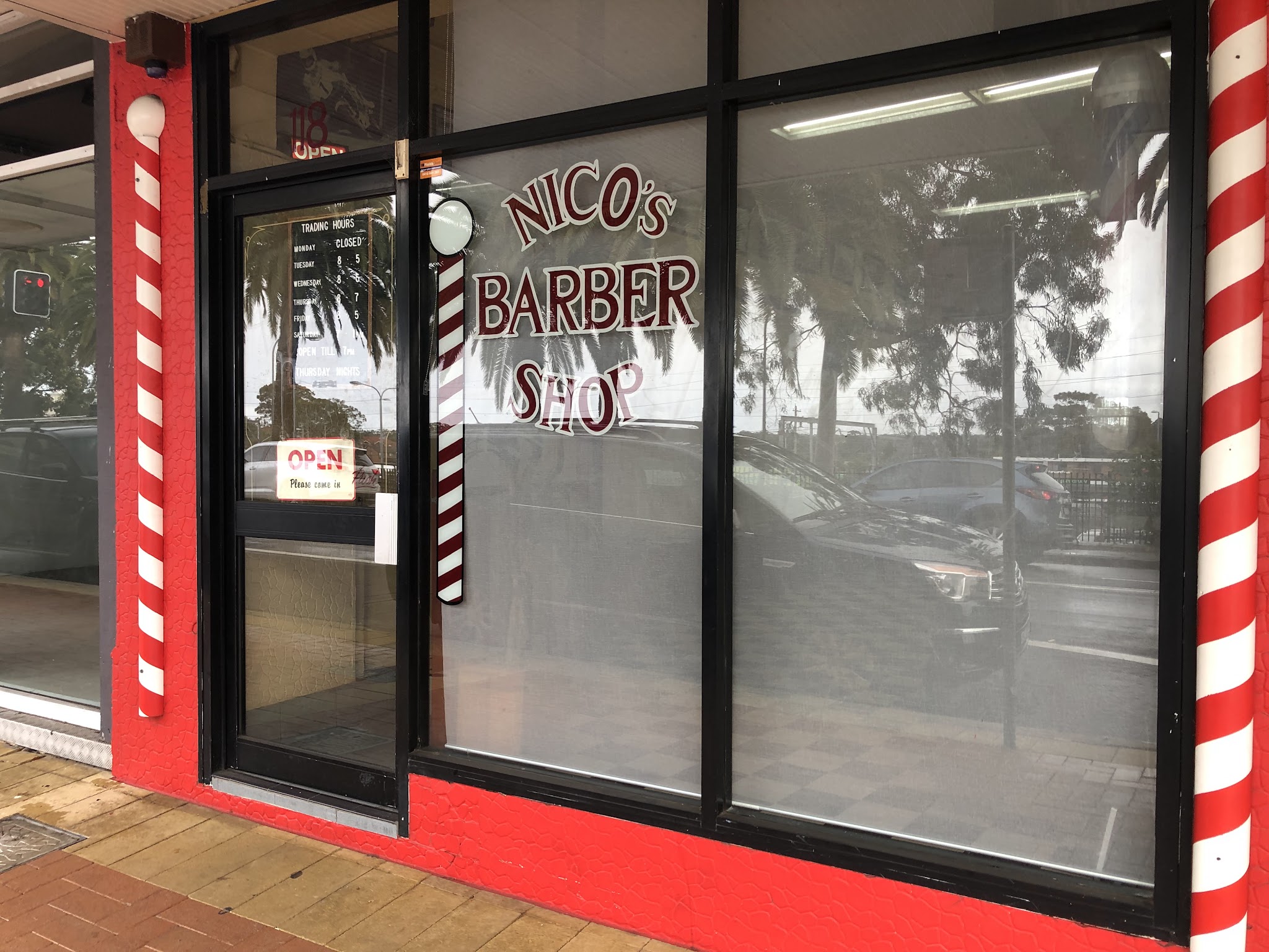 The red shopfront of Nico's Barber Shop on the Pacific Highway in Wyong, with barber poles either side of the window