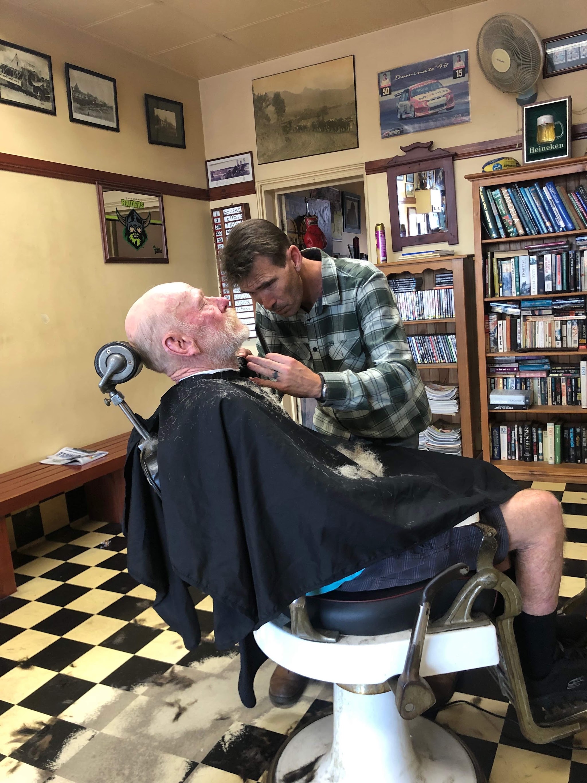 A barber trimming an older customer's beard in the reclining chair at Nico's Barber Shop