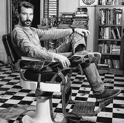 Black and white photograph of a man seated in the shop's cast iron barber chair
